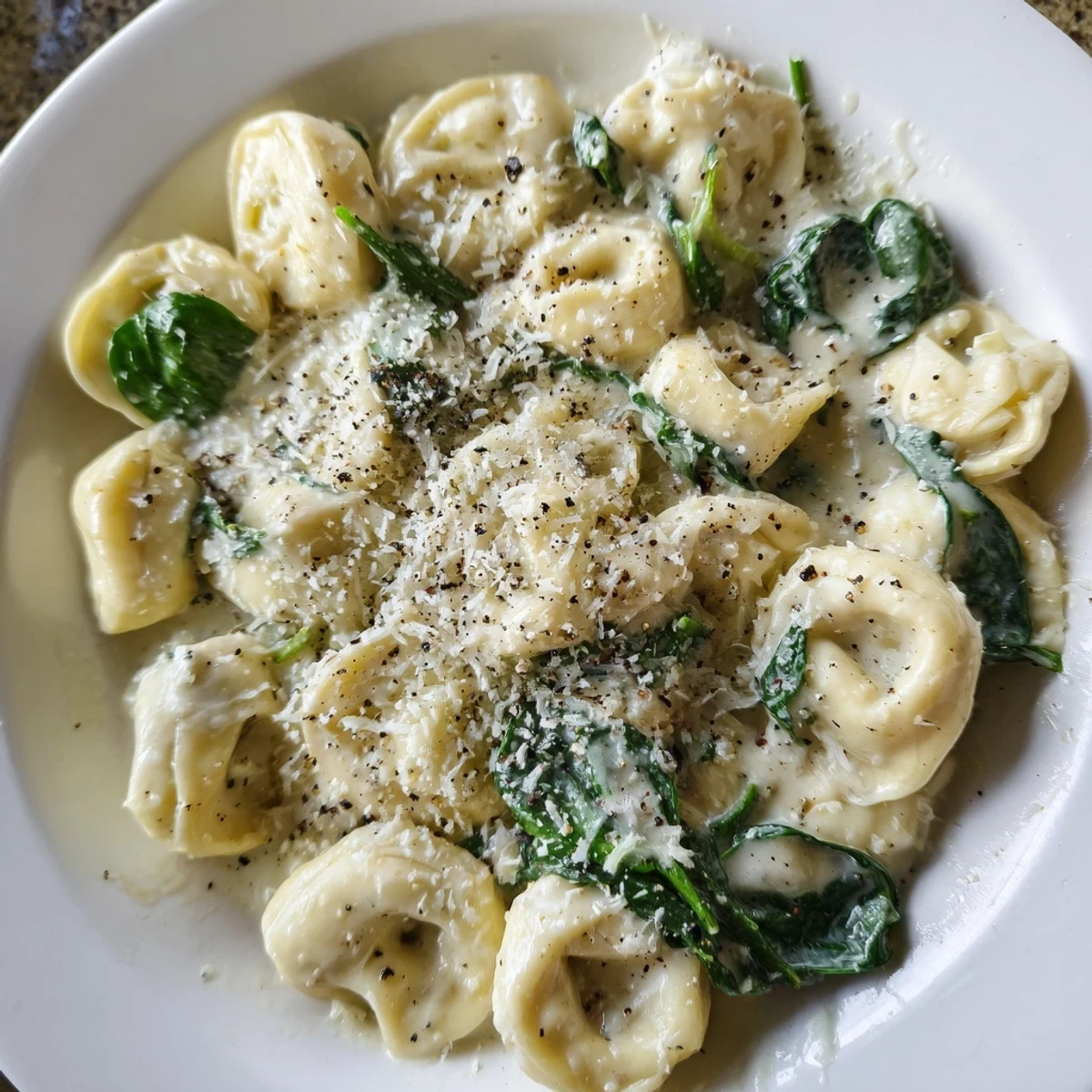 Homemade Creamy Spinach Alfredo Tortellini: Creamy, cheesy, perfect pasta garnished with fresh parsley and pepper.