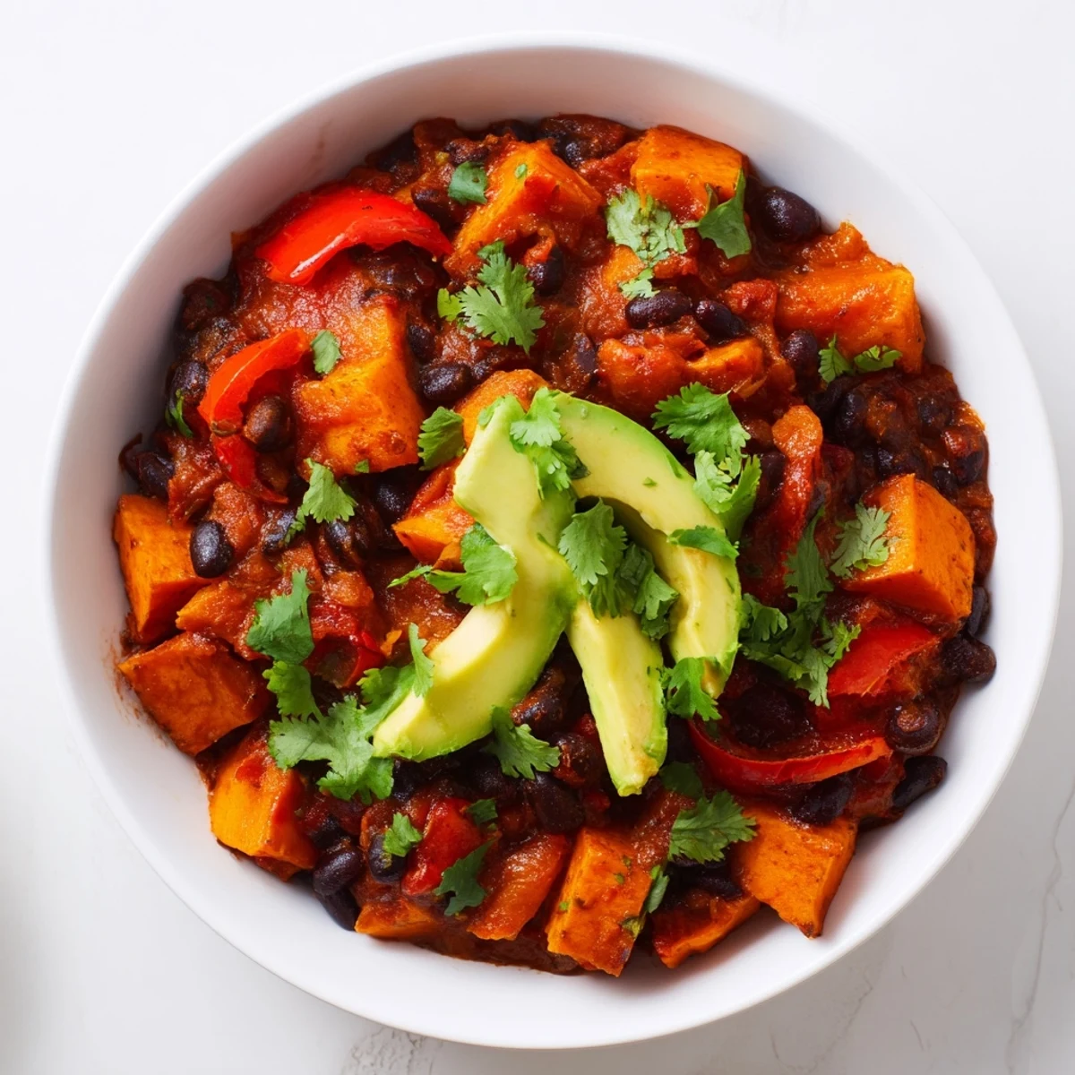 Steaming bowl of Sweet Potato & Black Bean Chili, garnished with cilantro, ready to serve.