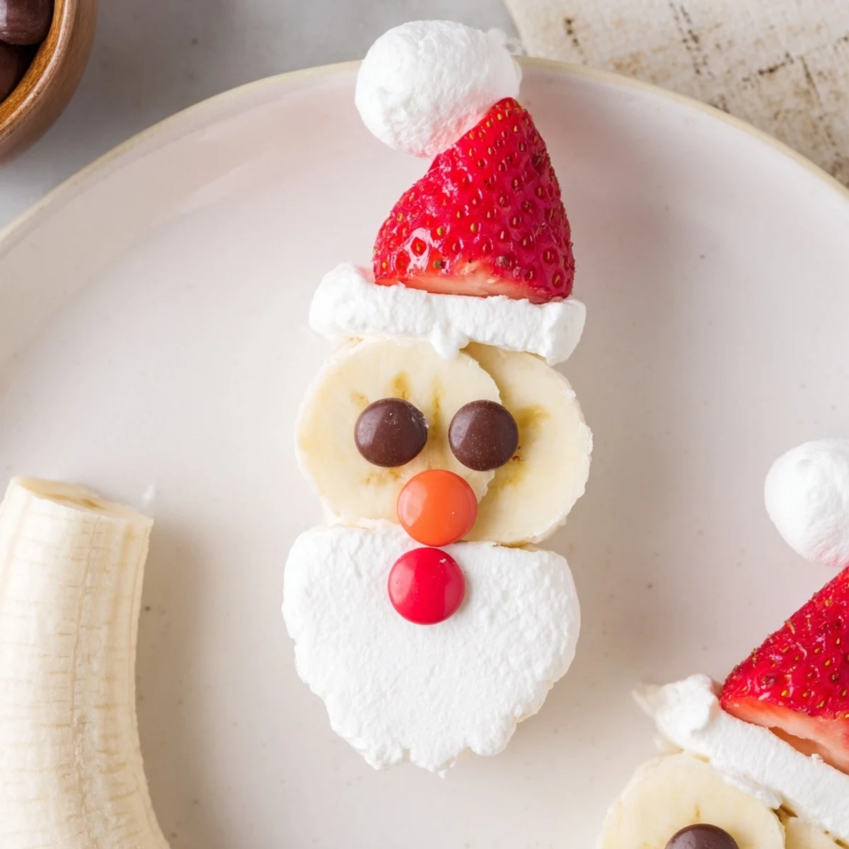 Bright, healthy Banana Santa Snack Sticks presented, with a strawberry Santa hat and chocolate chip eyes ready for kids.