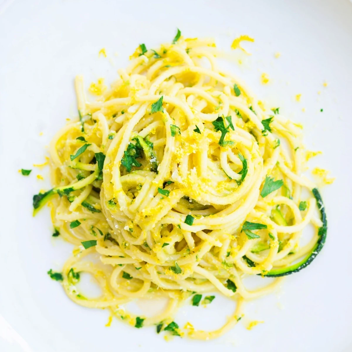 Overhead view of a white bowl filled with Lemon Zucchini Pasta, featuring bright lemon zest, al dente spaghetti, and crisp zucchini ribbons glistening with olive oil.  