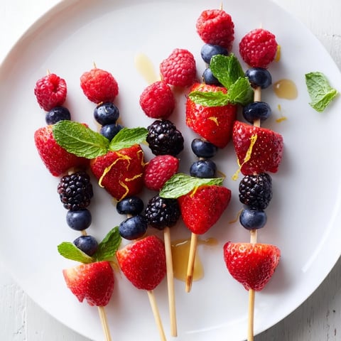 Vibrant fruit skewers showcase juicy, red strawberries, plump blueberries, and refreshing mint with every bite.