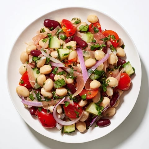 Image depicts a colorful Dense Bean Salad with Prosciutto, topped with fresh herbs, ready to be served.