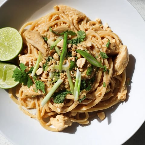 Steaming Thai Peanut Chicken Pasta, a savory dish garnished with fresh herbs and peanuts.