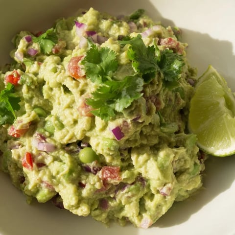 A bowl of creamy Edamame Guacamole, speckled with red onion, ready for dipping chips.