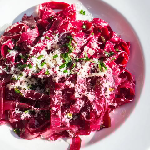 Beet Noodle Pasta, a beautiful magenta hue, served with fresh herbs and Parmesan, ready to enjoy.