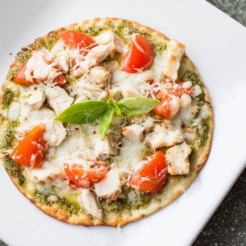 Freshly baked Chicken Pesto Pizza with melted mozzarella, juicy tomato slices, and a golden thin crust on a wooden board.