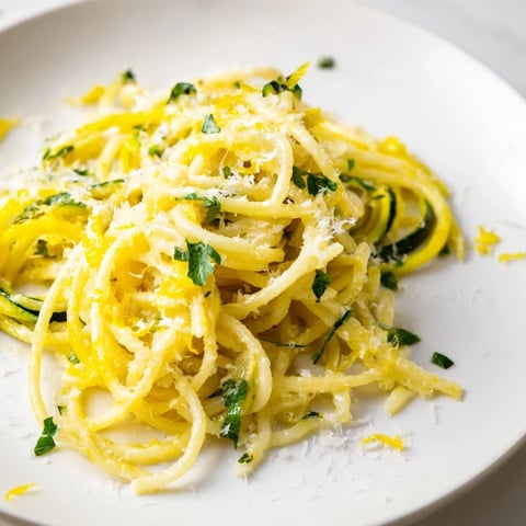 A close-up of Lemon Zucchini Pasta with golden spiralized zoodles coated in a glossy lemon butter sauce, topped with fresh parsley and shaved Parmesan.  