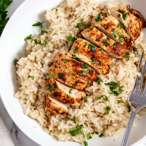 Golden-grilled chicken breast slices rest atop fluffy garlic butter rice, garnished with fresh parsley and lemon wedges on a rustic plate.