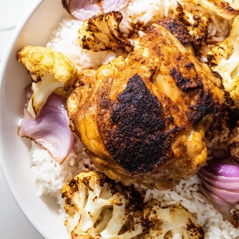 Golden roasted chicken thighs and cauliflower florets seasoned with paprika on a sheet pan, served over fluffy basmati rice with lemon wedges.