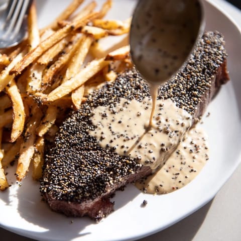 Juicy Classic Peppercorn Ribeye drizzled with creamy sauce and served alongside crispy fries.  
