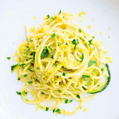 Overhead view of a white bowl filled with Lemon Zucchini Pasta, featuring bright lemon zest, al dente spaghetti, and crisp zucchini ribbons glistening with olive oil.  
