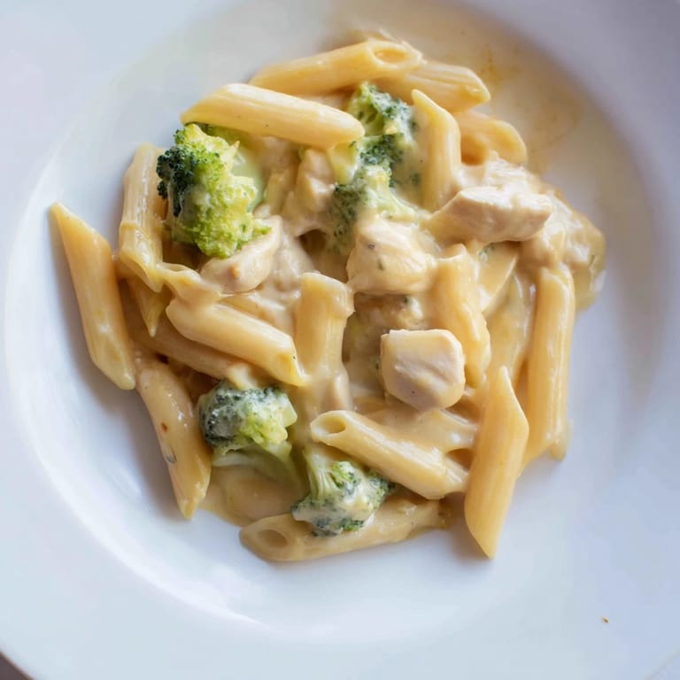 A close-up view of cheesy Chicken Broccoli Cheddar Pasta, showcasing rich sauce coating penne, broccoli, and golden-brown chicken pieces.