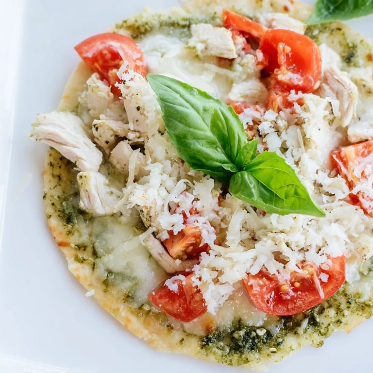 A rustic serving of Chicken Pesto Pizza featuring tender chicken, creamy mozzarella, and bright tomato on a crisp, thin crust.