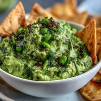 Creamy edamame guacamole with fresh cilantro served alongside crispy golden pita chips.  